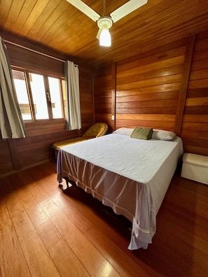 A room with wooden paneling, a bed with a white bedspread, a chair, and a ceiling fan. - Stone House Azul (Great location) (Domingos Martins)
