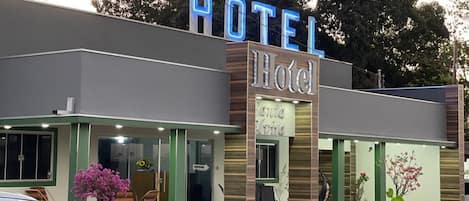 A hotel with a prominent 'HOTEL' sign, a glass entrance, and outdoor seating.
