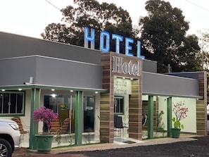 Un hotel con un llamativo letrero que dice 'HOTEL', entrada de vidrio y asientos al aire libre.