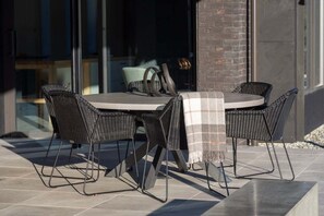 Een terras met een ronde tafel en vier stoelen, een plaid op de tafel, en een bakstenen muur op de achtergrond.