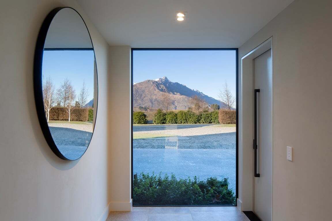 A hallway with a large mirror and a door leading to a view of a mountain and a parking area.