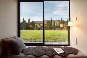 A room with a large window, a sofa with cushions, and a lamp on the wall. - Speargrass Villa | Luxury | Hot Tub | Pool (Queenstown)
