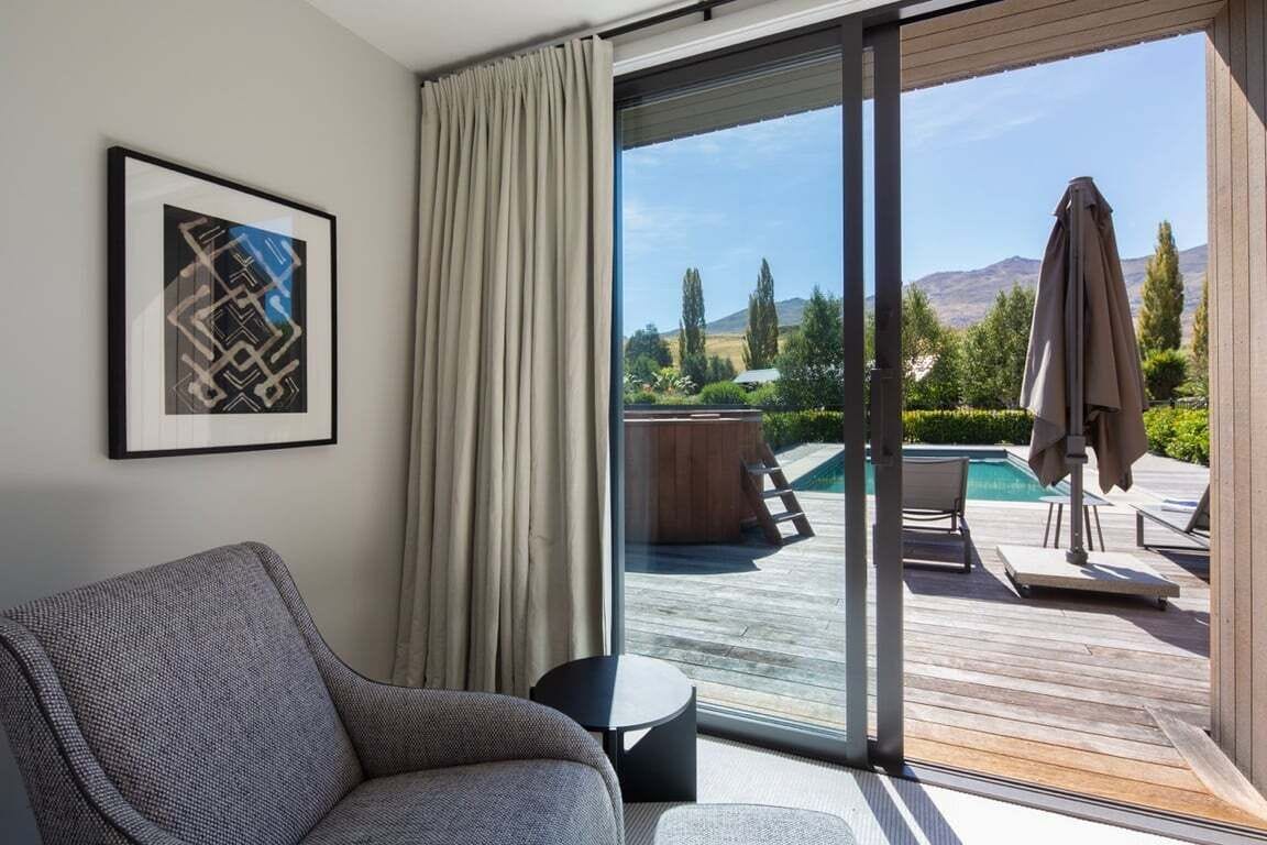 Una camera moderna con un'ampia porta scorrevole in vetro che dà su una terrazza esterna con piscina e sedie a sdraio.