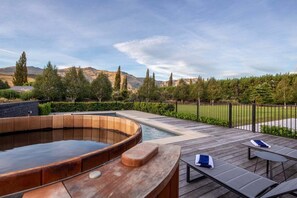 A hot tub on a wooden deck with lounge chairs and a view of a landscaped garden and mountains. - Speargrass Villa | Luxury | Hot Tub | Pool (Queenstown)