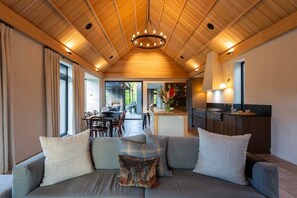 A modern living room with a sofa, a chandelier, and a view to the dining area. - Speargrass Villa | Luxury | Hot Tub | Pool (Queenstown)