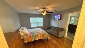 A bedroom with a bed, a sofa, a ceiling fan, a TV, and a window with blinds. - Contractor Preferred: Extended Stay Ready w/ On-Site Laundry & Great Rates (Panama City)