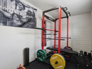 A gym with a red squat rack, weight plates, and a motivational poster on the wall. - New Relaxing 3 Bedroom Desert Oasis with Sparkling Pool! (Tucson)
