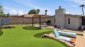 Un patio trasero con un patio, una parrilla y una piscina.