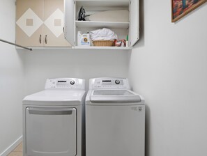 A laundry area with two front-loading washing machines and a shelf above containing laundry supplies. - New Relaxing 3 Bedroom Desert Oasis with Sparkling Pool! (Tucson)