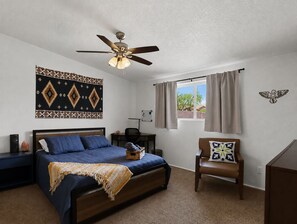 A bedroom with a bed, a chair, a desk, a ceiling fan, and a window with curtains. - New Relaxing 3 Bedroom Desert Oasis with Sparkling Pool! (Tucson)