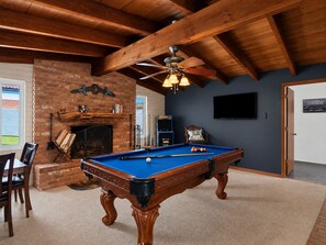 A pool table in a room with a brick fireplace, wooden ceiling beams, and a television mounted on the wall. - New Relaxing 3 Bedroom Desert Oasis with Sparkling Pool! (Tucson)