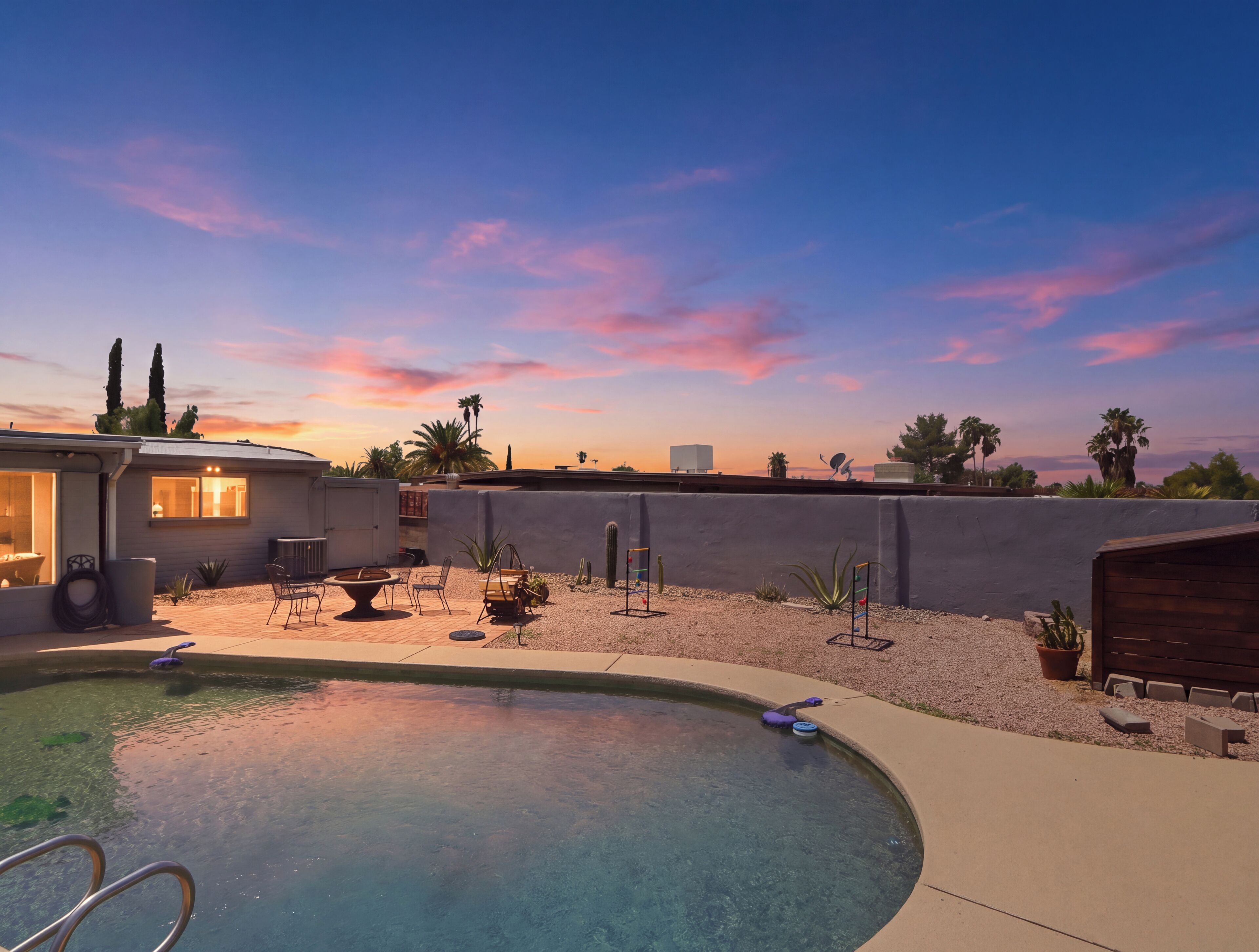 A backyard with a swimming pool, patio furniture, and a view of the sunset.