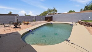 Una piscina con cubierta de madera, zona de barbacoa y pared de piedra.