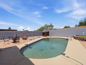 Ein Schwimmbad mit Holzterrasse, Grillplatz und einer Steinmauer.