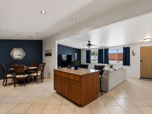 A modern kitchen with a central island, dining area with chairs, a sofa, and a TV. - New Relaxing 3 Bedroom Desert Oasis with Sparkling Pool! (Tucson)