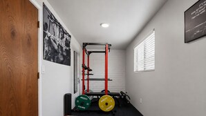 Un gimnasio en casa con una estructura para sentadillas, discos de pesas y mancuernas.