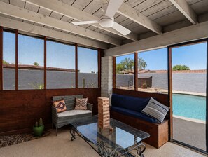 A room with a glass coffee table, two sofas with cushions, a ceiling fan, and a view of a swimming pool. - New Relaxing 3 Bedroom Desert Oasis with Sparkling Pool! (Tucson)