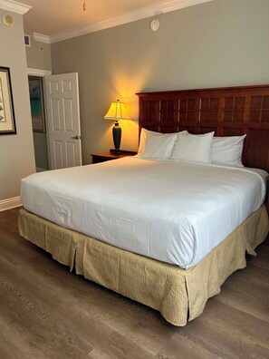 A neatly made bed with a wooden headboard, a bedside lamp, and a door to the left. - Beautiful condo with amazing view located in Emerald Grande at the Harborwalk. (Destin)