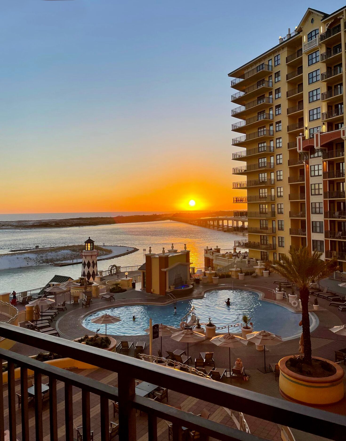 A hotel with a pool, a beach view, and a sunset.