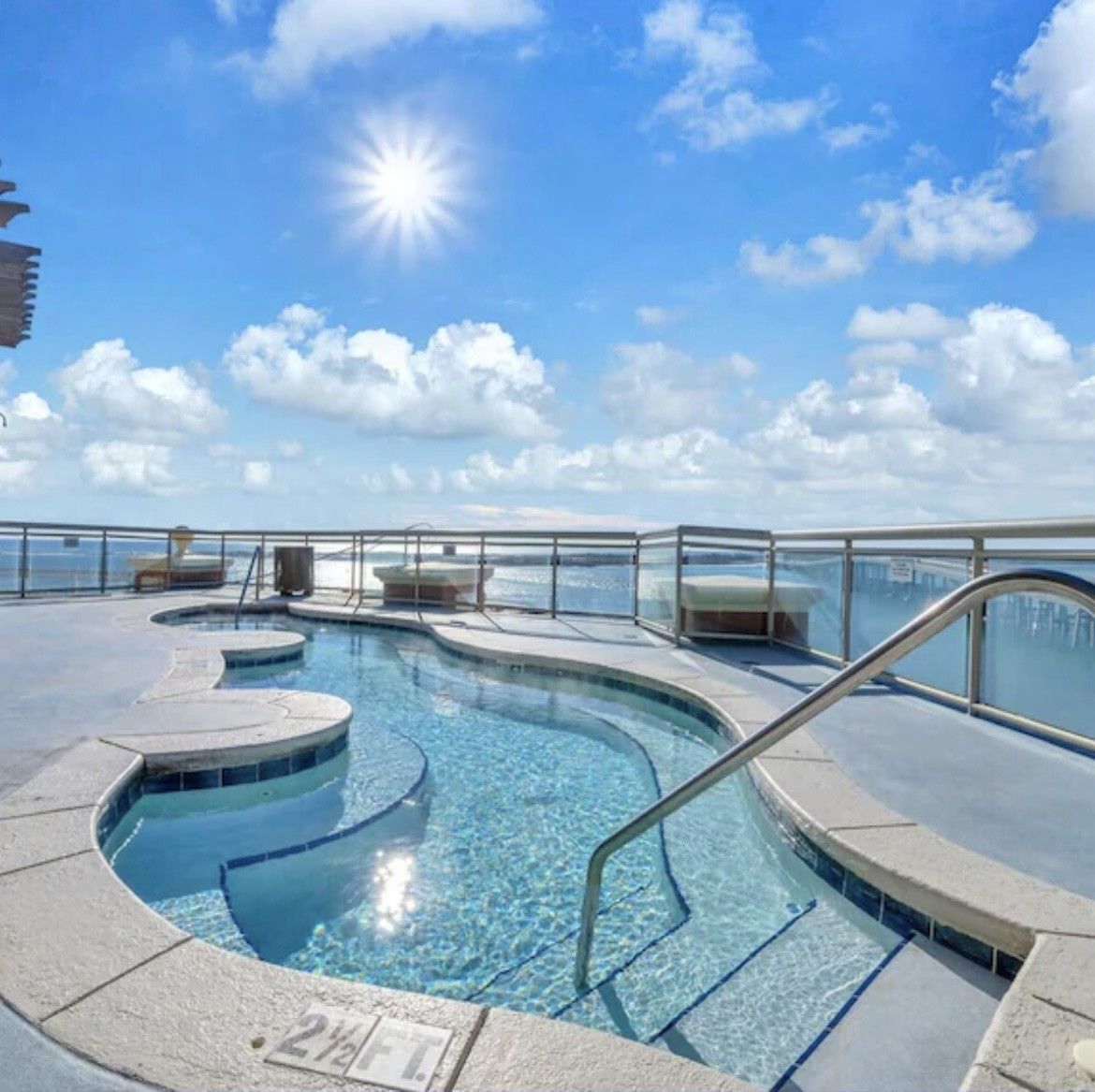 A pool with a glass barrier and a sunlit sky.