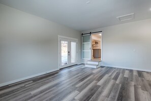 Ein geräumiges Zimmer mit grauem Fischgrätparkett, einer Schiebeglasdoor, die zu einem Außenbereich führt, und einer eingebauten Regaleinheit in der Ecke.