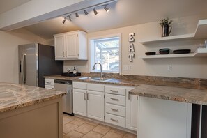 A modern kitchen with white cabinetry, a stainless steel refrigerator, a dishwasher, and a granite countertop. - Mountain Views of the San Juans. Great outdoor living, near bike, hike and swim. (Ridgway)