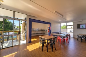 A spacious room with large windows, a wooden floor, and a kitchen area with a microwave and stove. - Urban Lounge Sleeepery Dorm (Rotorua)