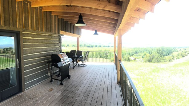 A wooden deck with a grill and chairs, overlooking a grassy landscape.