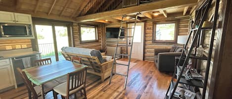 Interior de una cabaña con comedor, sofá, escalera y una escalera de caracol que lleva a un altillo.