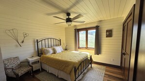 A bedroom with a bed, bedside table, nightstand, chair, and a window with curtains.
