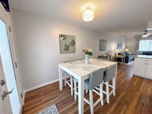 A dining area with a white table and chairs, a vase with flowers, and a ceiling light fixture. - Beach Breeze - Across from Beach (Panama City)