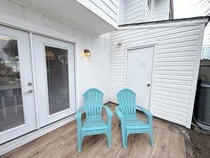 A white exterior with a sliding glass door, a small porch with two chairs, and a light fixture. - Beach Breeze - Across from Beach (Panama City)