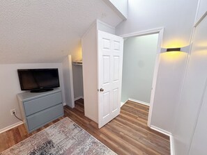 A room with a television on a dresser, a door leading to another room, and a light fixture on the wall. - Beach Breeze - Across from Beach (Panama City)