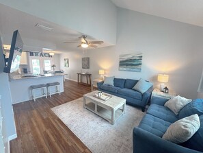 A modern living room with a blue sofa set, a coffee table, and a kitchen area with a bar. - Beach Breeze - Across from Beach (Panama City)