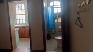 Habitación con piso de madera, ventana con vistas, puerta que da a un baño y un gancho fijado a la pared.