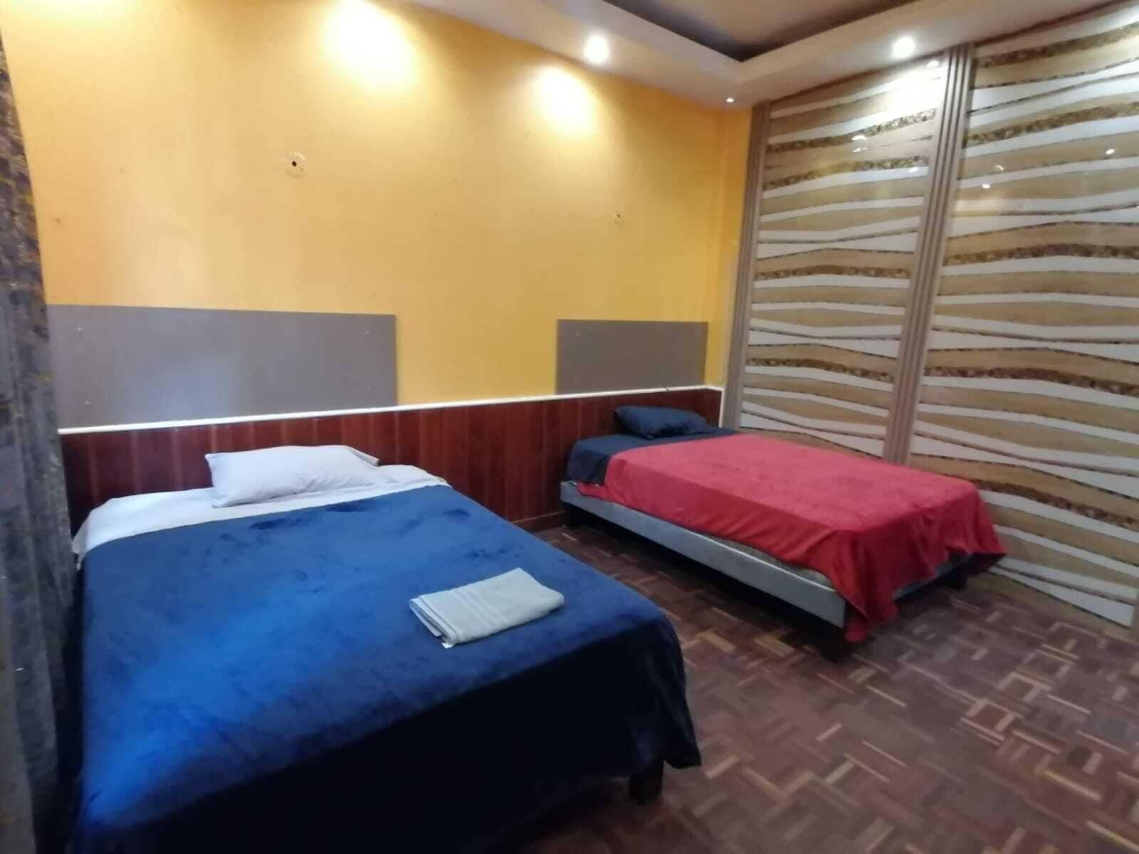 A room with two beds, wooden headboards, a patterned wall, and a herringbone floor.