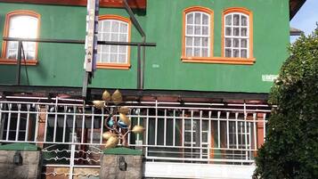 Un edificio verde con marcos de ventana naranja, una reja de metal y una escalera que lleva a la entrada.