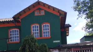 Un edificio con fachada verde, dos ventanas de marco rojo y un árbol en primer plano.