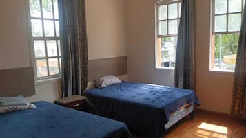 Una habitación con dos camas, piso de madera y ventanas amplias con cortinas.