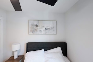 Ein modernes Schlafzimmer mit einem Bett, einem Nachttisch, einer Lampe und einem Gemälde an der Wand.