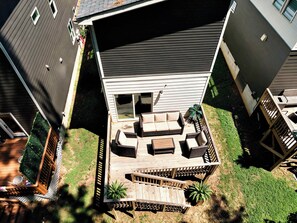 Eine Terrasse mit Gartenmöbeln, ein kleiner Garten und ein Haus mit dunklem Dach und weißer Fassade.