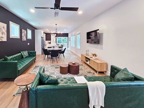Ein modernes Wohnzimmer mit einem grünen Sofa, einem Essbereich und einem an der Wand befestigten Fernseher.