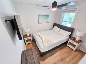 Une chambre à coucher avec un lit, des tables de chevet, un ventilateur de plafond, une fenêtre et un tableau au mur.