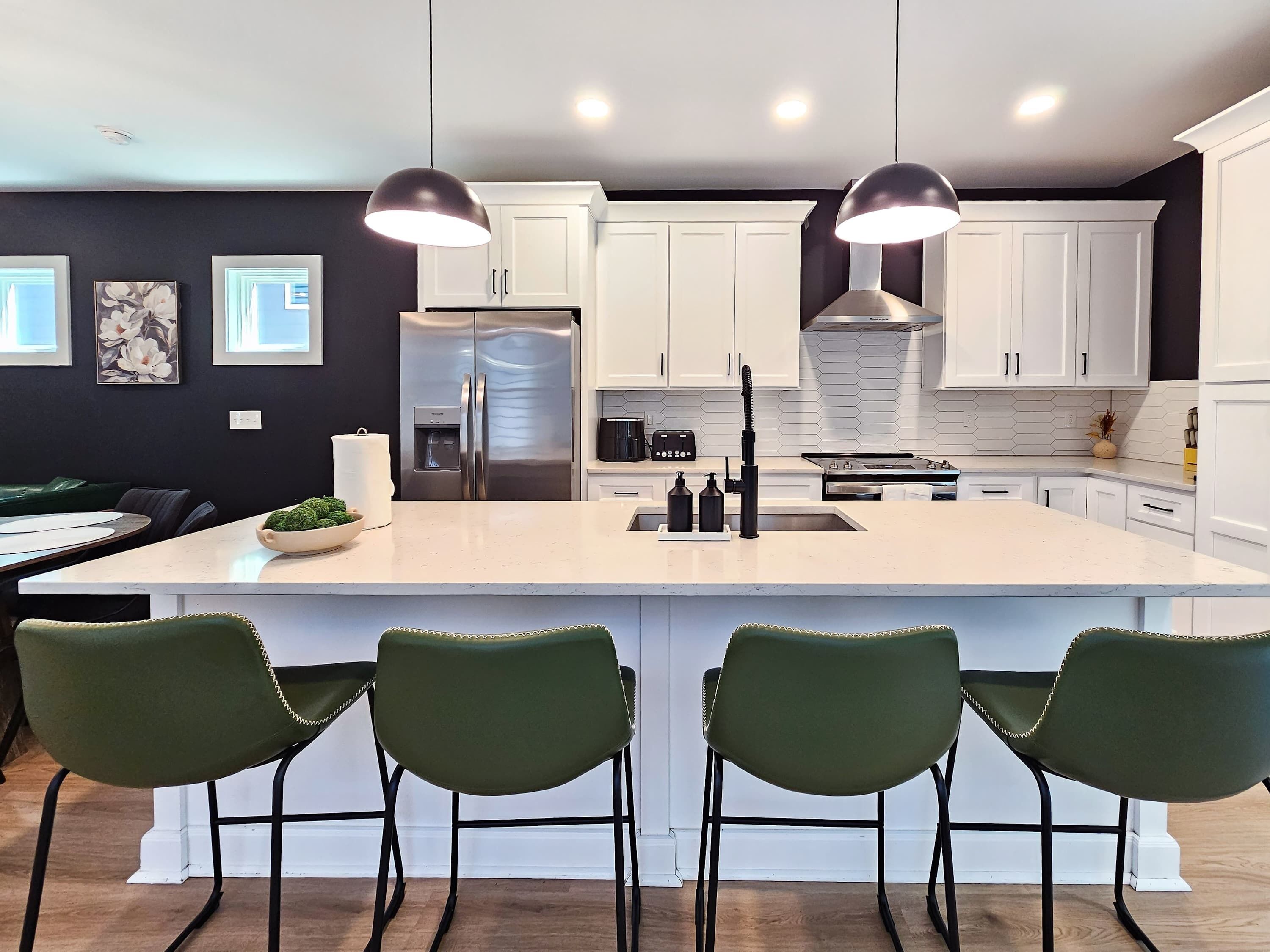 A modern kitchen with a central island, white cabinets, and green chairs.
