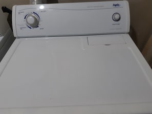 Vista frontal de una lavadora blanca con un panel de control que incluye un dial y un botón pulsador.