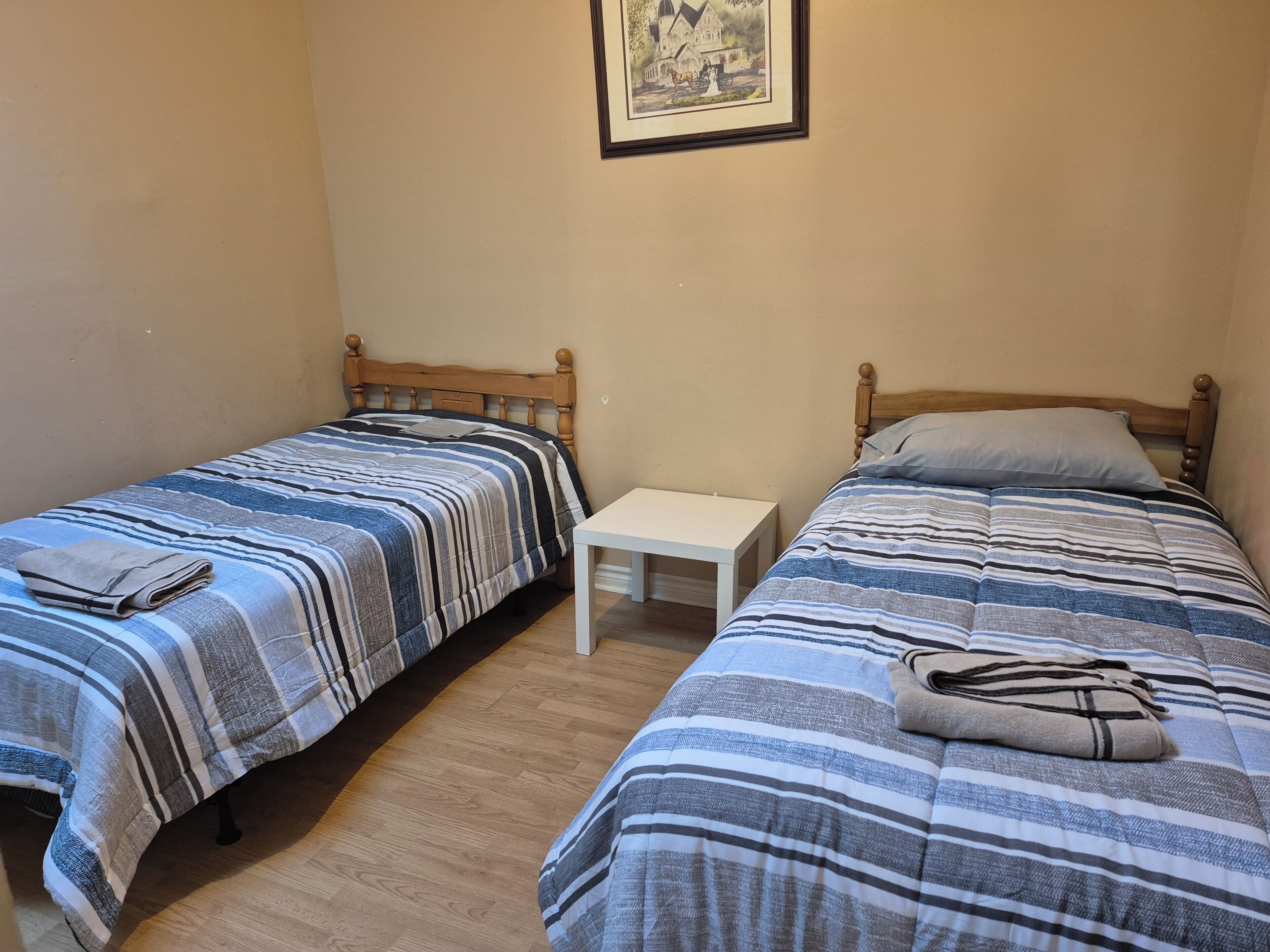 A room with two single beds, a small white table, and a framed picture on the wall.