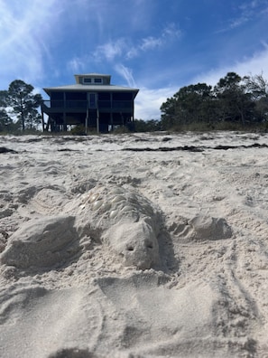 A sandy beach with footprints leading to a two-story building with a flat roof. - 4 bedroom beach front beach house (Alligator Point)