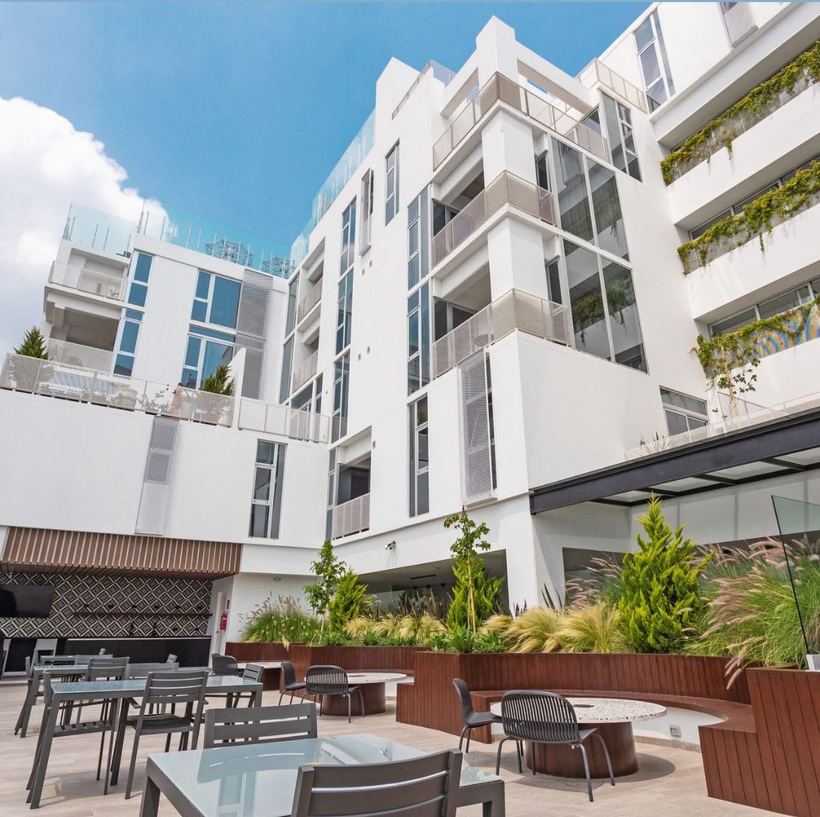 A modern building with multiple balconies, outdoor seating, and greenery.