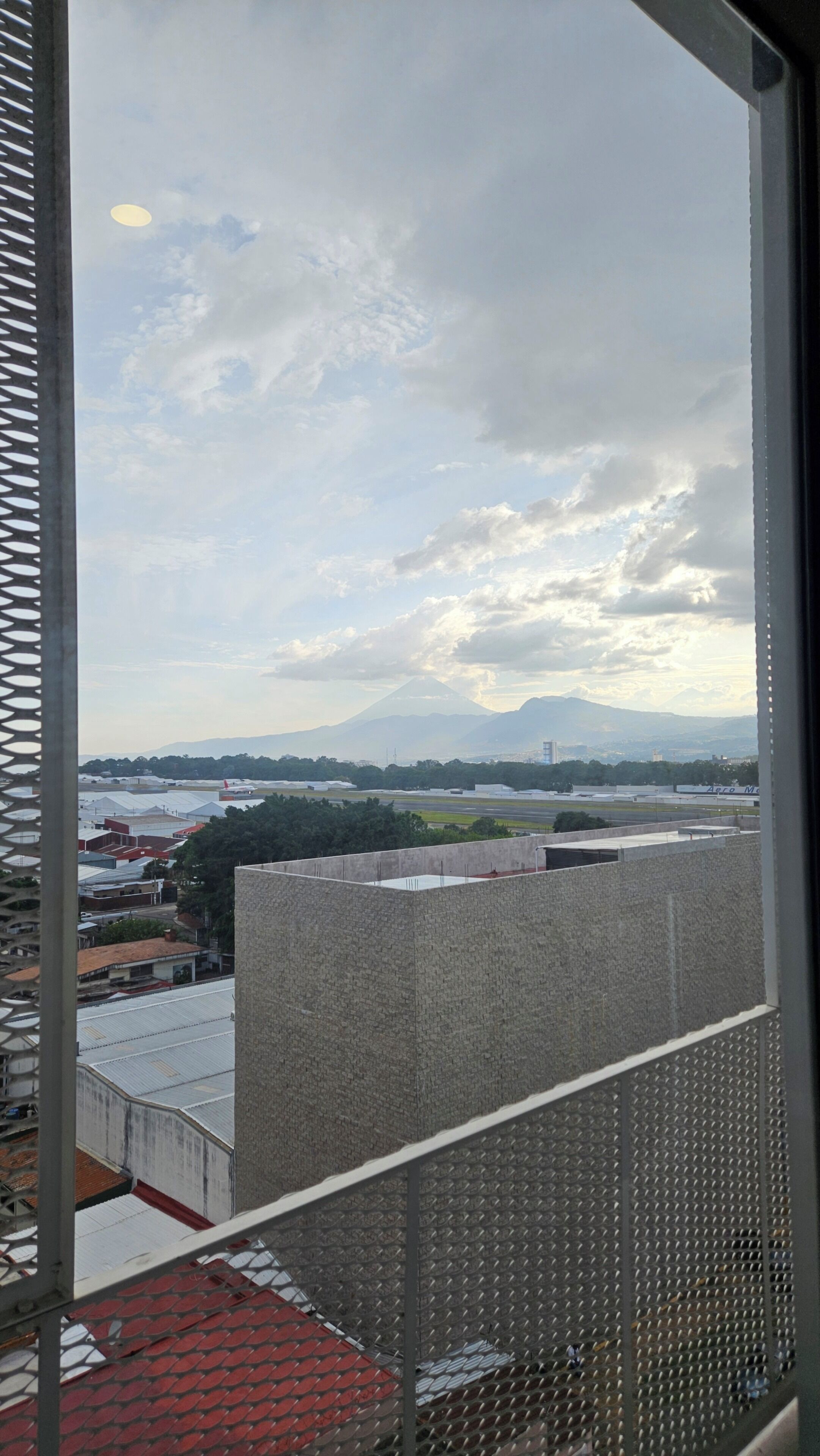 Vista desde una ventana hacia un paisaje urbano con edificios y una montaña distante.
