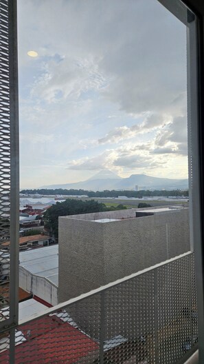 Vista da janela sobre a paisagem urbana, com edifícios e uma montanha ao longe.